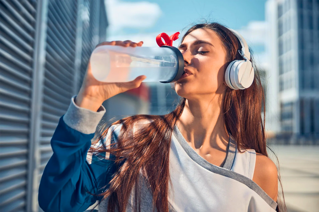 Woman drinking electrolyte water from bottle outdoors during workout